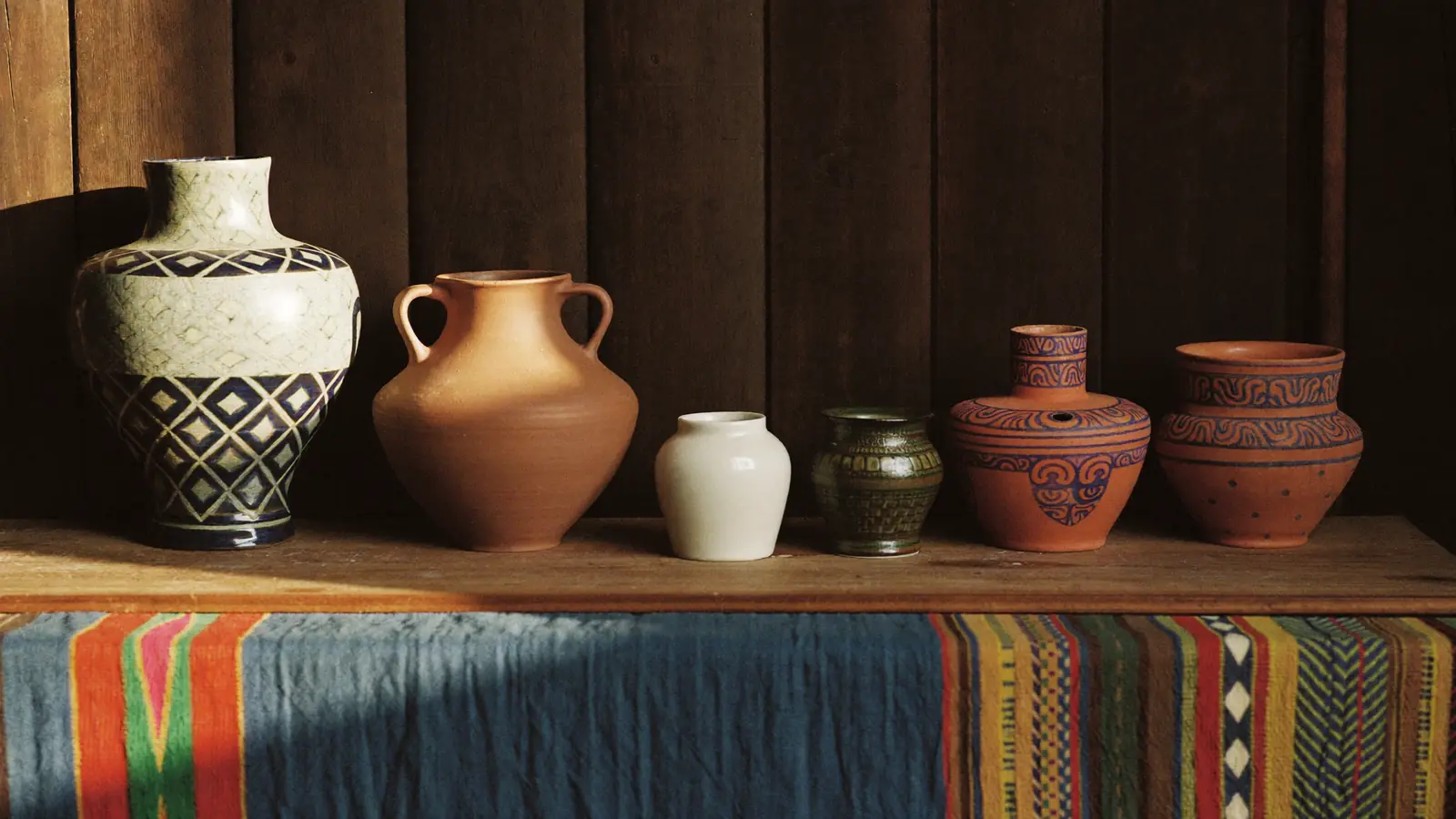 A row of handmade celadon and terracotta vessels on a teak table