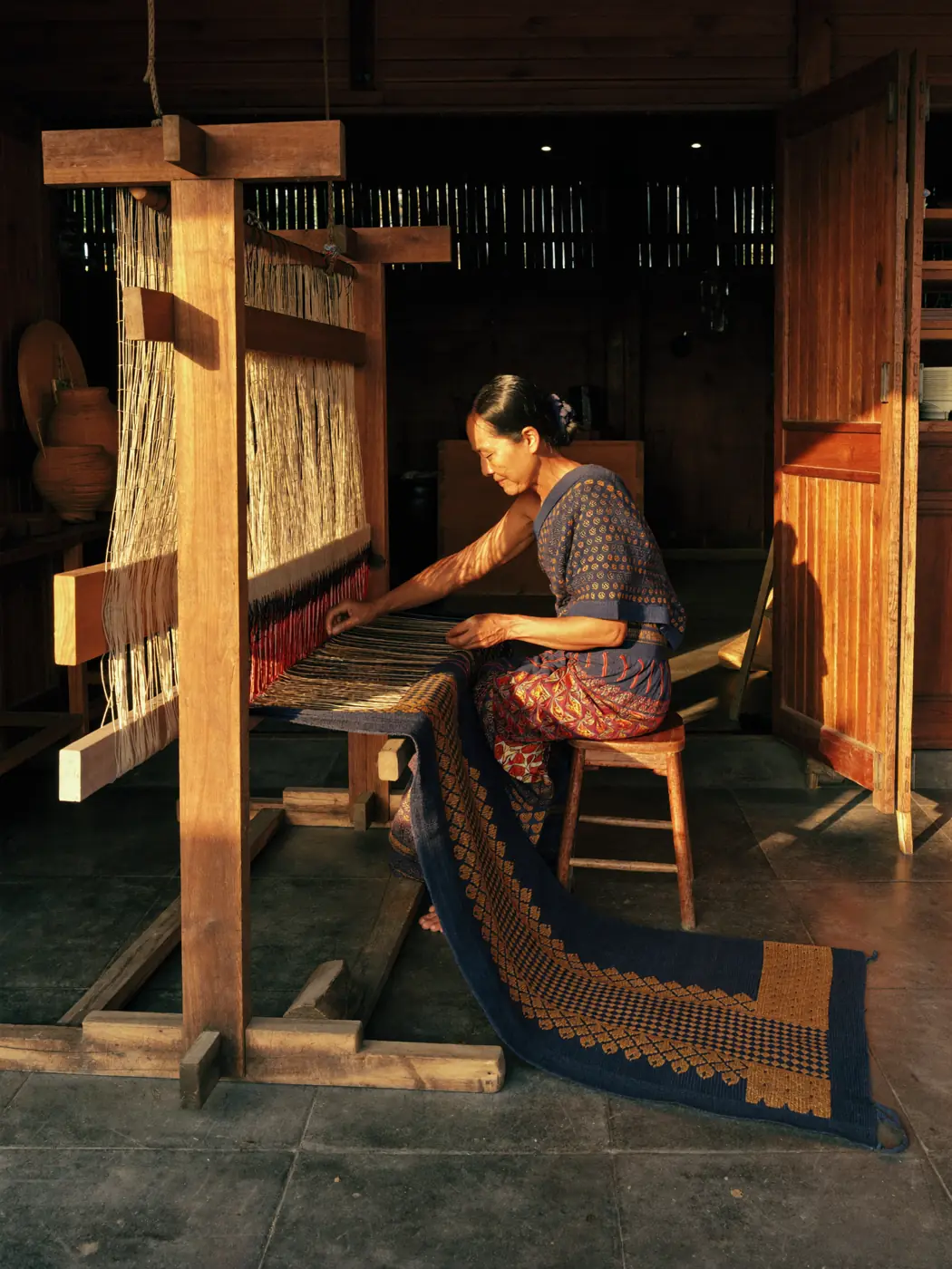 A weaver passing the shuttle through indigo and gold warp threads