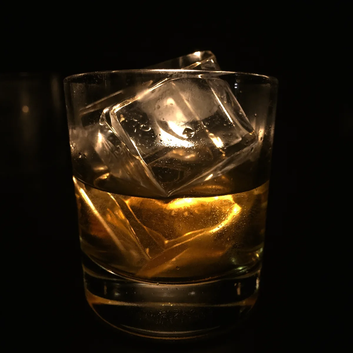 Clear ice in a heavy tumbler catching a single warm light