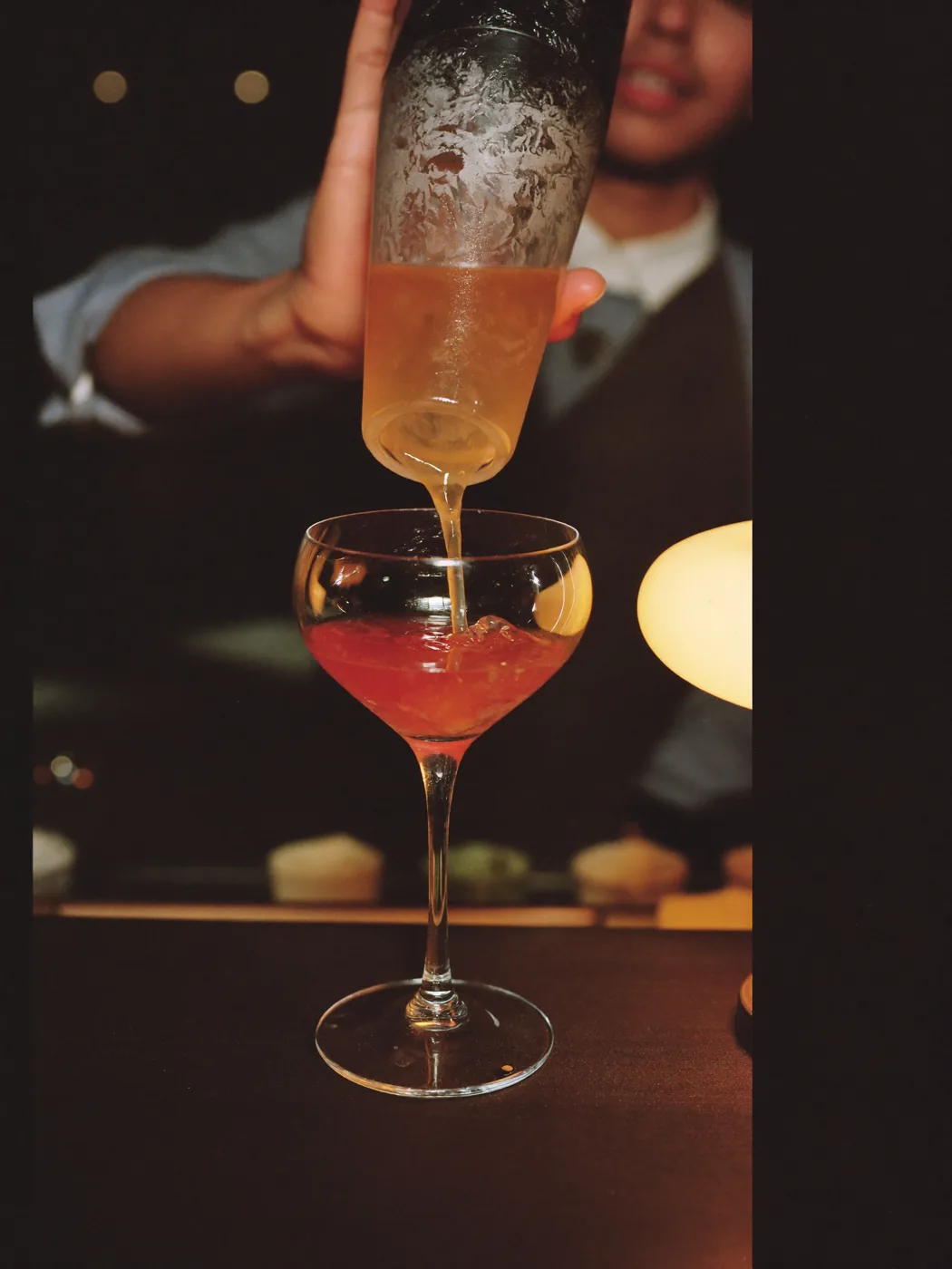 A bartender straining a cocktail under a warm lamp